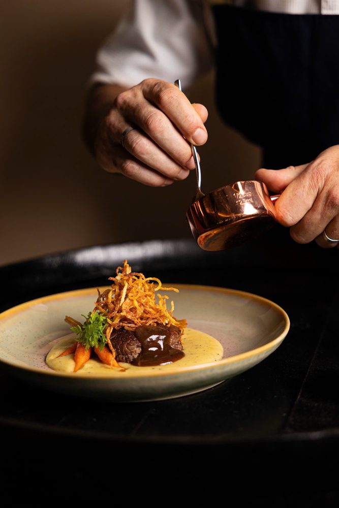 Chef pouring sauce over main course